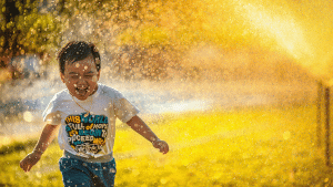 Young boy running through water from sprinklers